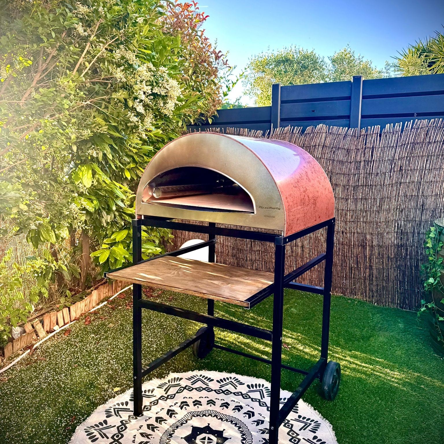 Forno Pizza Party Ispirazione Grande rame antico su carrello con ruote in giardino, vista frontale con botte decorativa sullo sfondo