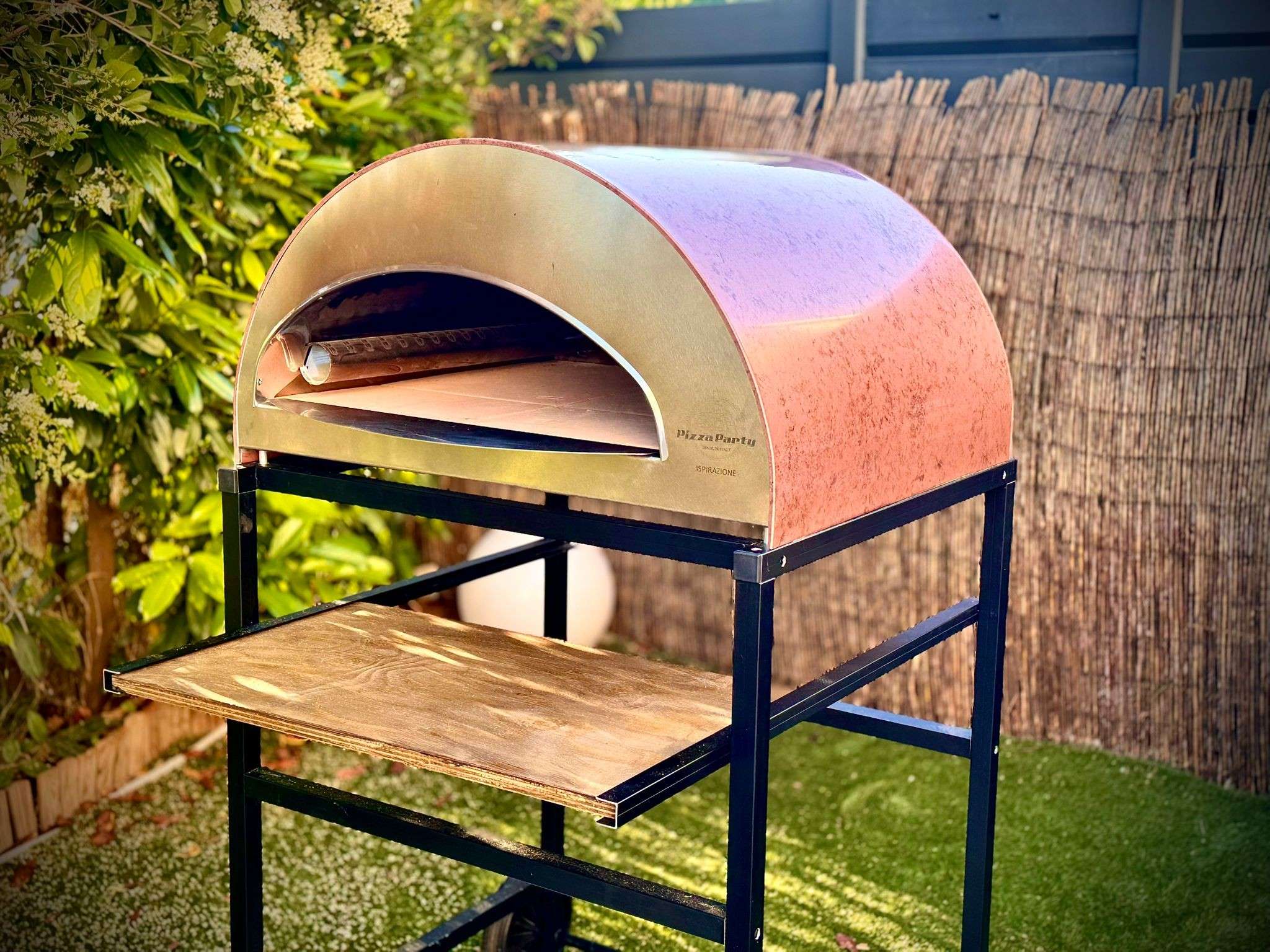 Large Inspirational Antique Copper Pizza Party Oven with a 60x70cm cooking surface, side view in a garden featuring the text 'NEW 70x60cm'