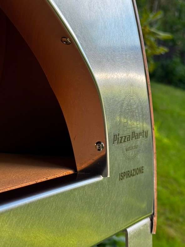 Large shiny silver Pizza Party Inspiration oven with lit burner, front view showing visible flames