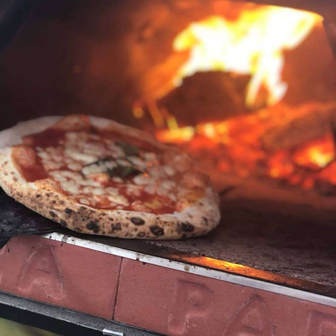 Houtgestookte pizzaoven Pizza Party 70x70 'Pietra' op een witte tafel in de tuin, voorzijde met rookkanaal aan de achterzijde