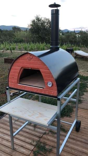 Large wood-fired Pizza Party pizza oven on an aluminum wheeled stand on a wooden terrace with countryside in the background